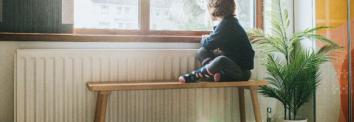 Kind sitzt auf Bank und schaut aus Fenster